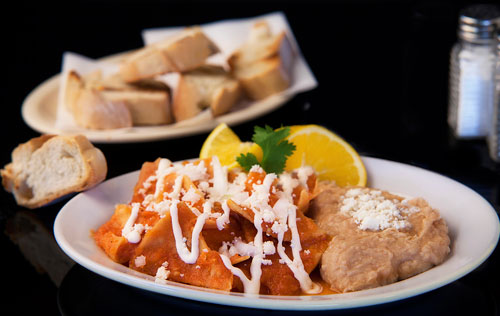 Red Chilaquiles with refried beans, bread and orange