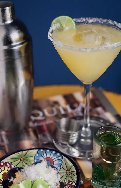 Margarita Gold junto a un mezclador de bebidas y un shot de tequila